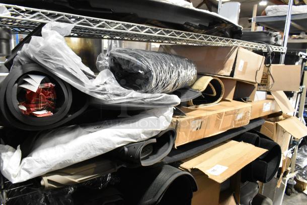 Lot of various items including car floor mats, rolled cloths, and boxed goods on metal shelves in a warehouse setting.