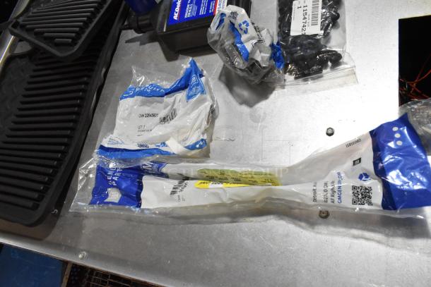 Various items including ACDelco Versatrak fluid bottle, sealed floor mats, and labeled parts, all in a black poly bin.