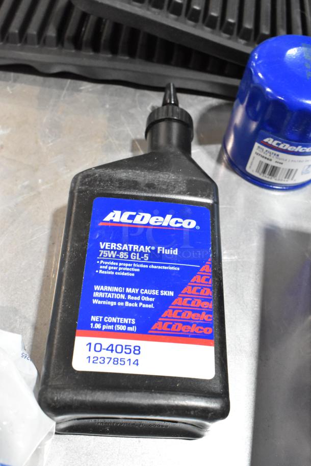 Lot includes ACDelco Versatrak Fluid, 75W-85 GL-5, 500ml bottle, and black floor mats in a poly bin; items appear in good condition.