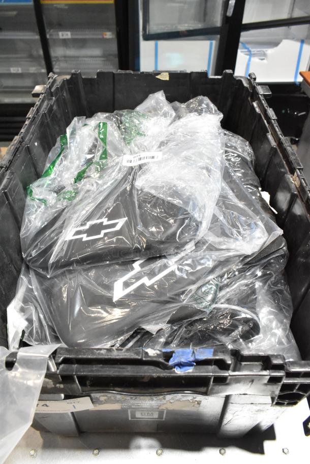 Black poly bin containing various items, including Chevy logo mats wrapped in plastic and an oil filter. Items appear new.