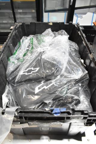 Black poly bin containing various items, including Chevy logo mats wrapped in plastic and an oil filter. Items appear new.