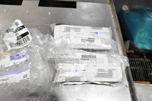 Lot of various items including GM wheel locks, stick shift, in black poly bin; labels indicate part numbers and GM branding.