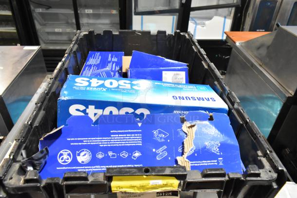 Lot of miscellaneous items in black poly bin including Samsung CLT-C504S/XAA toner cartridges, visible labels and instructions.