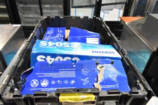Lot of miscellaneous items in black poly bin including Samsung CLT-C504S/XAA toner cartridges, visible labels and instructions.