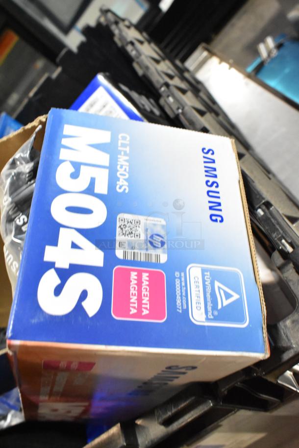 Samsung CLT-C504S/XAA toner cartridges in black poly bin. Box displays magenta color indicator and TÜV Rheinland certification.