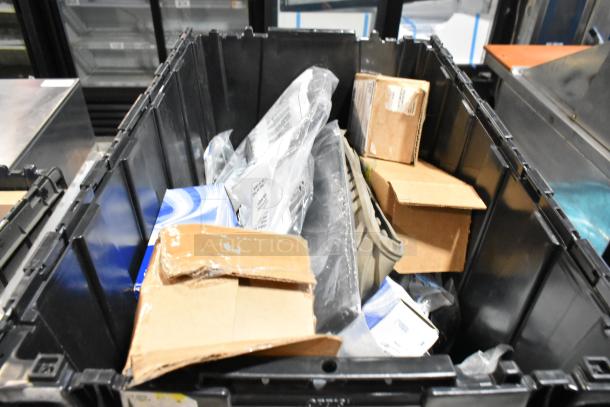 Black poly bin containing assorted items including floor mats, cardboard boxes, and plastic packaging. Various conditions.