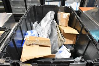 Black poly bin containing assorted items including floor mats, cardboard boxes, and plastic packaging. Various conditions.