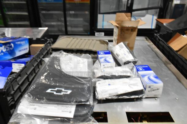 Lot of various items including black floor mats with Chevrolet logo, in black poly bin. Some items in original packaging.