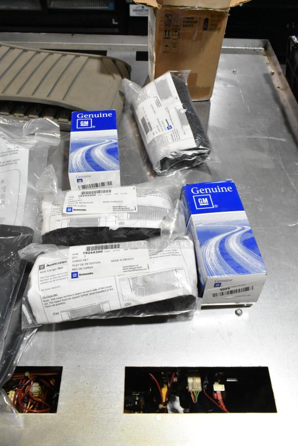 Lot of various automotive items including GM genuine accessories, floor mats, and cargo net in black poly bin.