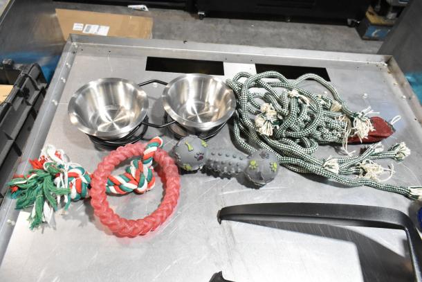 Lot of assorted dog toys and items in a black poly bin. Includes braided ropes, rubber chew toys, and stainless steel bowls.