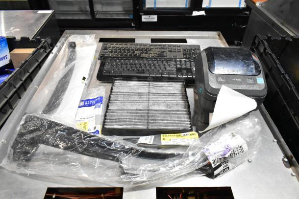 Lot of items in black poly bin, including ZP505 label printer and keyboards. Includes tags with part numbers and genuine parts label.