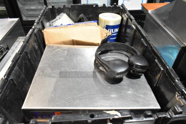 Black poly bin containing various items including headphones, packaging tape, and a cardboard box.