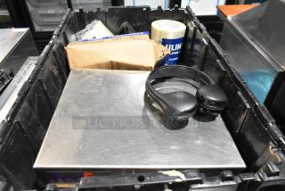 Black poly bin containing various items including headphones, packaging tape, and a cardboard box.
