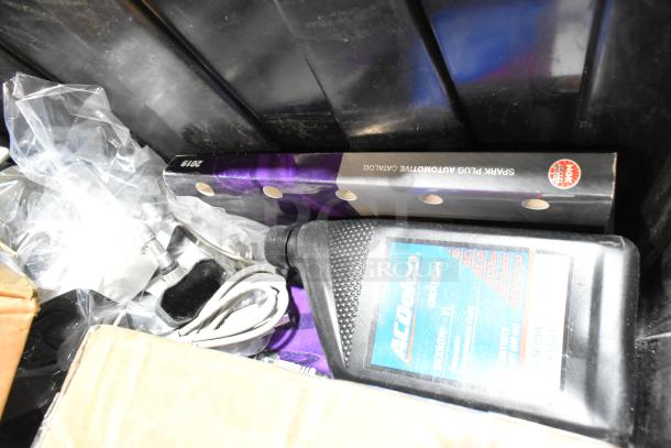 Lot of various items in black poly bin, including headphones, ACDelco fluid bottle, and 2019 spark plug catalog.