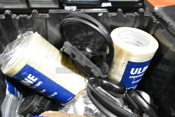 Lot of various items in black poly bin, including black headphones and Uline strapping tape rolls.