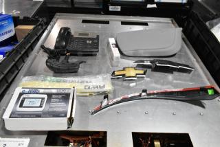 Lot of items including a black corded telephone, Chevrolet emblem, LockState thermostat, and other accessories in a poly bin.