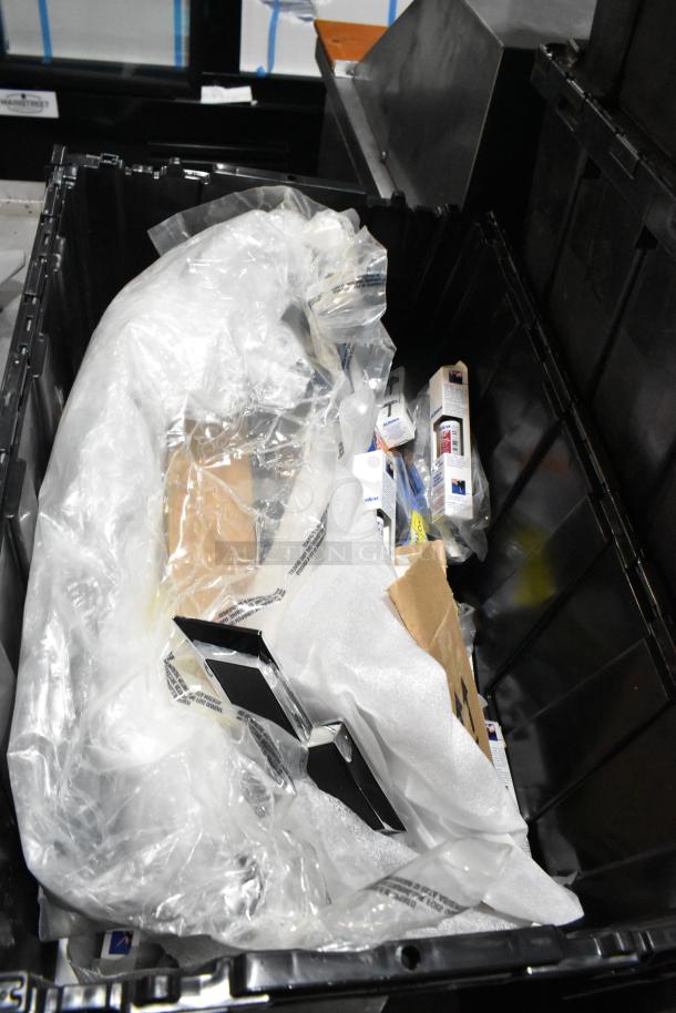 Black poly bin containing assorted items, including a corded telephone and thermometer, with packaging material.