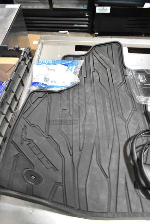 Lot of items in black poly bin, including floor mats with textured design and headphones. New condition.