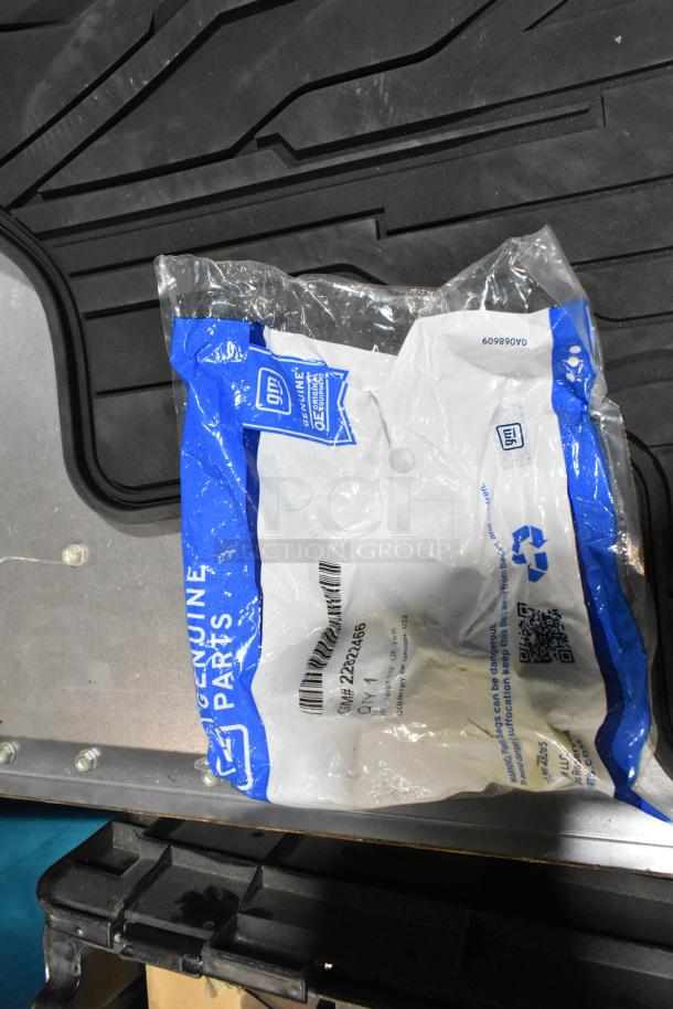Lot of various items including floor mats, headphones, housed in black poly bin. GM Genuine Parts bag visible on mats.