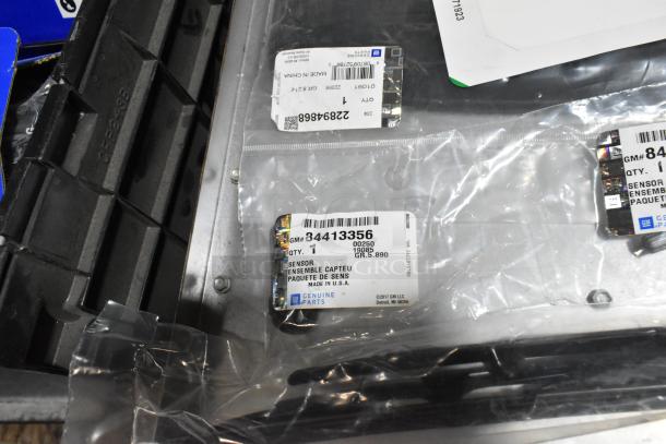 Assorted items in black poly bin, including floor mats and cable ties. GM sensors with labels, new condition.