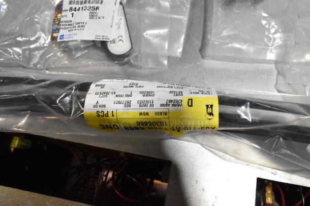 Assorted items including floor mats and cable ties packaged in a black poly bin. Tags display product codes and details.