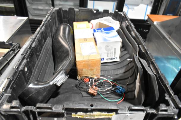 Black poly bin with assorted items including oil filter, GM 84126999 emblem, wires, and boxes. Mixed condition.