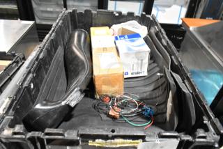 Black poly bin with assorted items including oil filter, GM 84126999 emblem, wires, and boxes. Mixed condition.