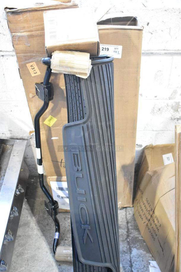 Buick floor mat, black rubber with branding, leaning against cardboard boxes; includes auction tag “219.”