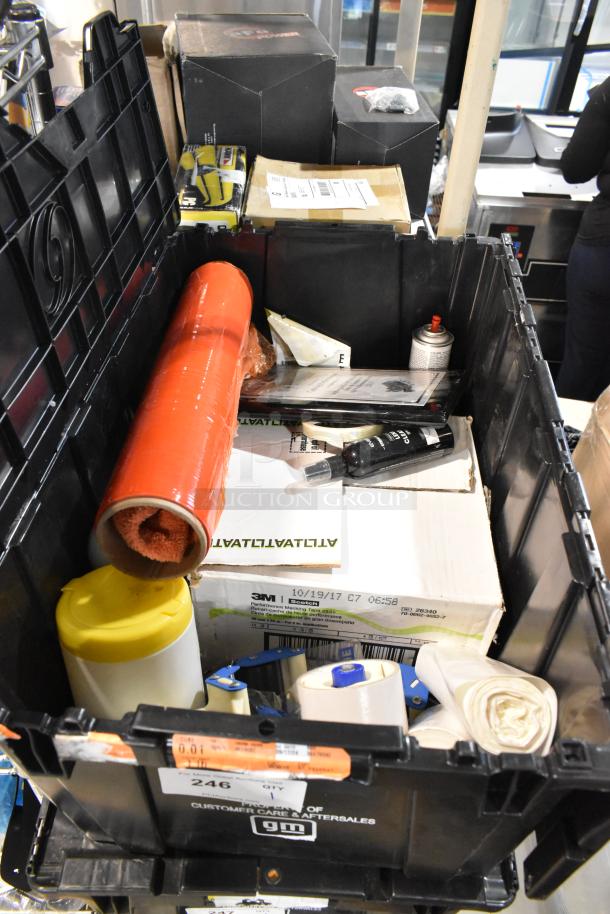 Black poly bin filled with various items including scissors, boxed items, red packaging roll, and labeled with "Customer Care Aftersales GM".