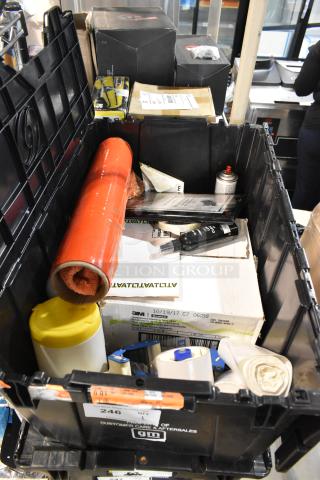Black poly bin filled with various items including scissors, boxed items, red packaging roll, and labeled with "Customer Care Aftersales GM".