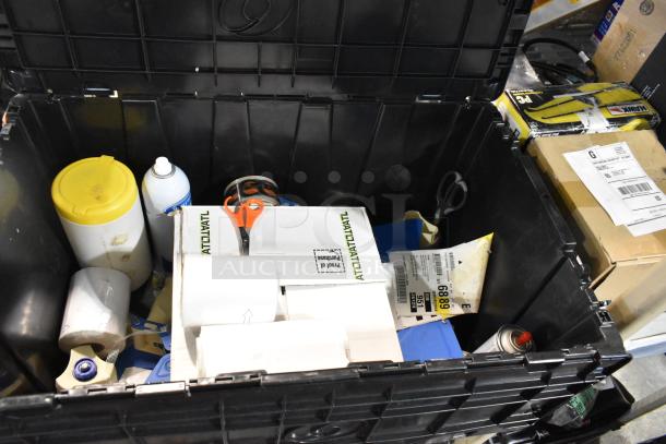 Black poly bin with assorted items including scissors, tape rolls, spray can, and paper towels. Moderate wear visible.