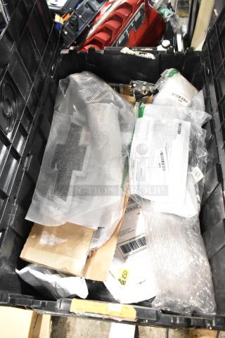 Lot of various items in black poly bin, featuring a Chevy emblem. Visible packaging includes labels and documents.