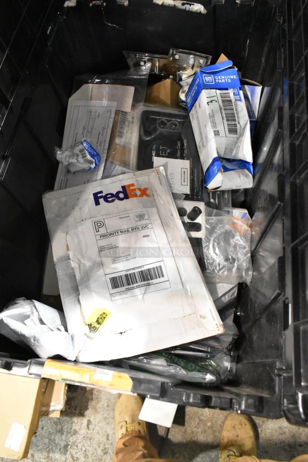 Black poly bin with various items, including a Chevy emblem, FedEx package, and GM Genuine Parts box. Mixed condition.