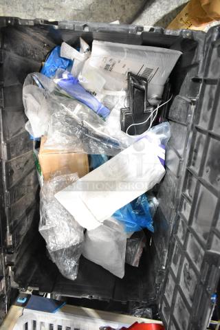 Black poly bin with various items including a Chevy emblem, packaging materials, and miscellaneous objects.