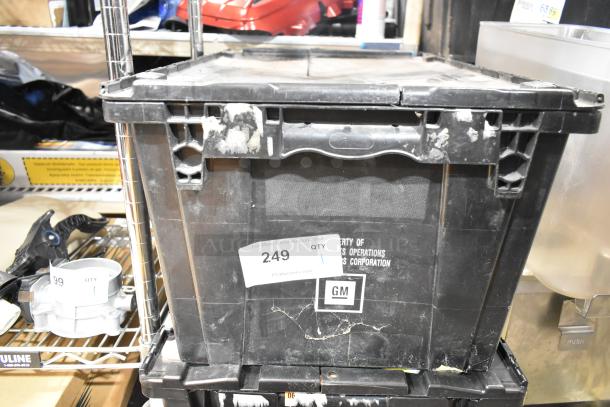Black poly bin containing various items including a Chevy emblem. Bin shows signs of wear. Label reads "Property of GM." Auction tag "249" attached.