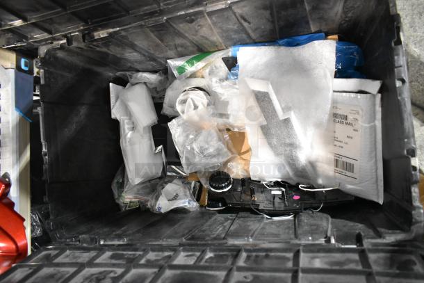 Black poly bin containing various items, including a Chevy emblem, assorted packages, and car parts.