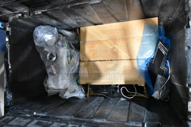 Lot of assorted items in used condition, including a Chevy emblem, packed in a black poly bin with cardboard and plastic wrap.
