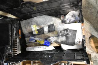 Lot of assorted items in a black poly bin, including a Corvette emblem. Contains various automotive parts and packaging.