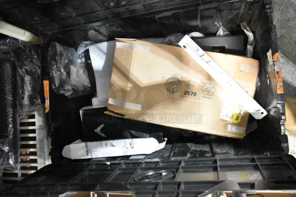 Lot of various items including a Corvette emblem, stored in a black poly bin, featuring assorted packaging materials and labels.