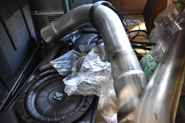 Assorted items including metal pipes and a Kicker subwoofer in mixed condition, labeled and wrapped in plastic.