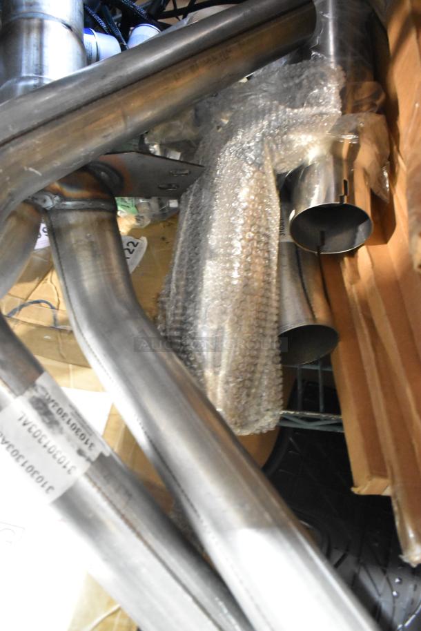 Nine metal pipes and accessories, some bubble-wrapped, in new condition. Labels visible, possibly for identification.