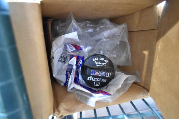 Box with Mobil 1 oil cap SAE 0W-40 Dexos label, mixed car items, new condition with packaging, key automotive parts.