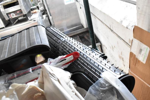 Tier lot with various items, including black car mats and coils, stacked in a warehouse setting. Items appear in used condition.