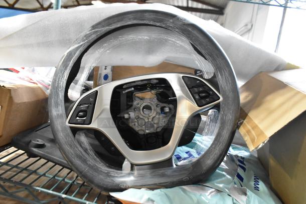 Modern car steering wheel with partially wrapped packaging, featuring control buttons and metal mount. Condition appears new.