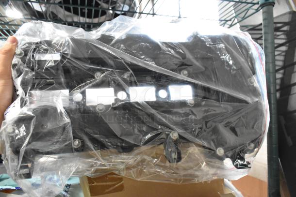 Plastic-wrapped black automotive part with bolt holes, part of a 3-item auction lot, condition appears new, no visible labels.