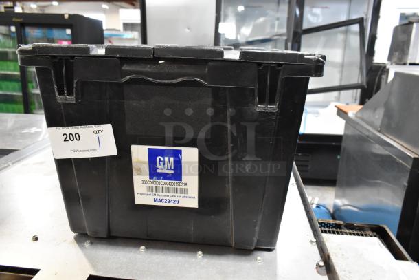 Black poly bin containing various items including wheel locks. Features GM label marked "Property of GM Customer Care and Aftersales".