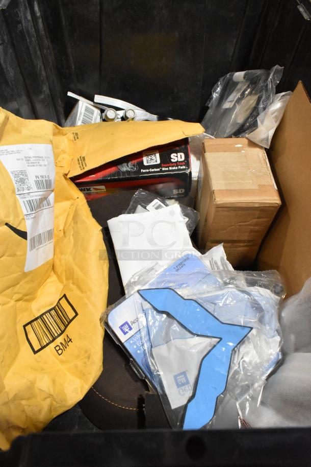 Lot of various items including wheel locks, disc brake pads, cardboard box, and mailer in black poly bin.