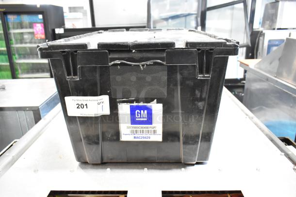 Black poly bin containing various items, including GM 20823543 front driver side fender ornament. Bin labeled with GM logo.