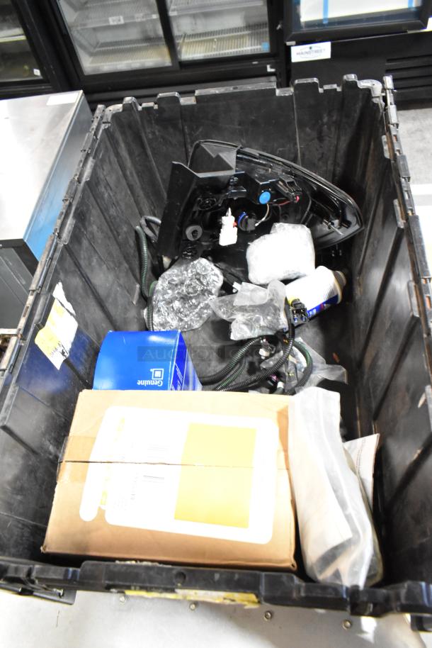 Black poly bin containing mixed items, including a GM front driver side fender ornament 20823543. Various packaging visible.