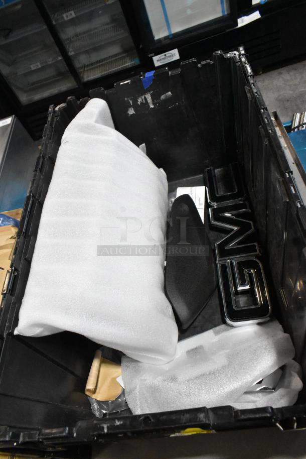 Black poly bin containing various items including a GMC emblem, wrapped items, and miscellaneous components.